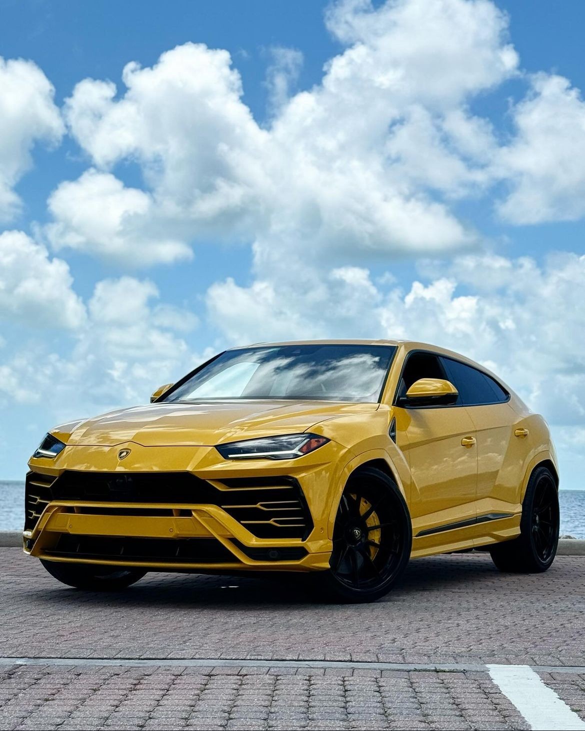 Yellow luxury SUV parked on a paved area with a cloudy blue sky background.